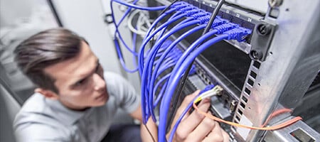 A man delicately holding a cable in a networking rack