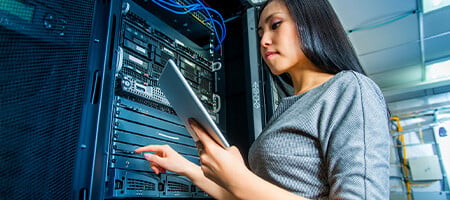 A woman holding a tablet while pointing on a server rack