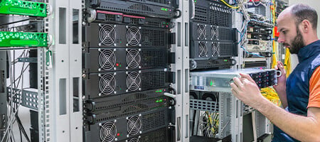 A man in a server room holding a half-inserted hardware in a rack